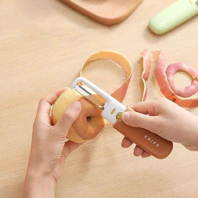 Person using a multifunctional fruit knife peeler to peel an apple on a wooden surface