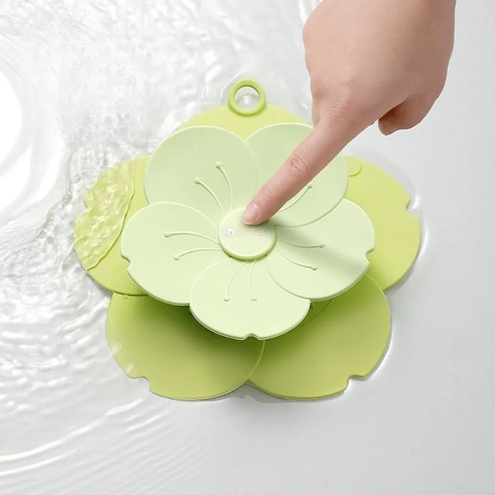 Green silicone drain cover for bathroom shaped like a flower being pressed by a finger