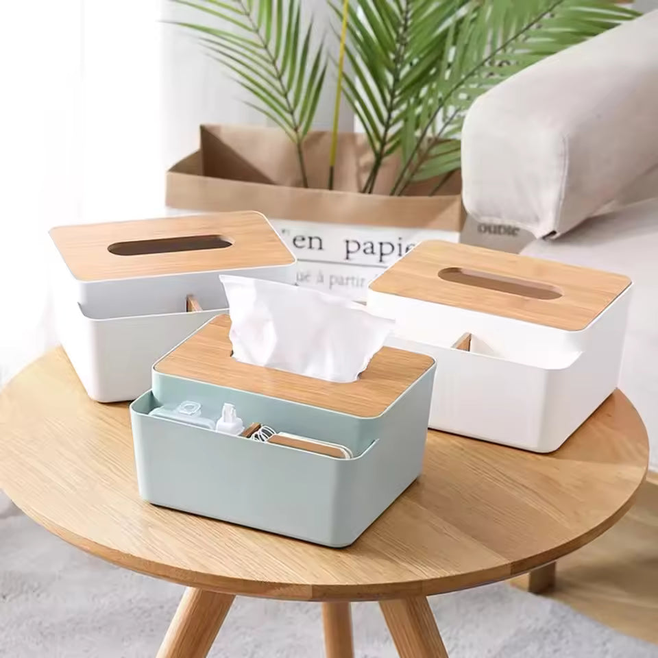 Three plastic tissue box with wooden lid in white and green on a round wooden table with plants in background