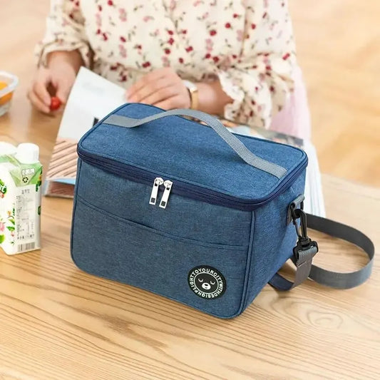 Blue Oxford cloth portable insulated lunch bag with gray handles and zipper on wooden table