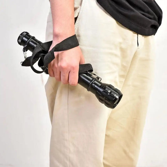 Portable outdoor flashlight for camping held in hand with wrist strap by person in beige pants