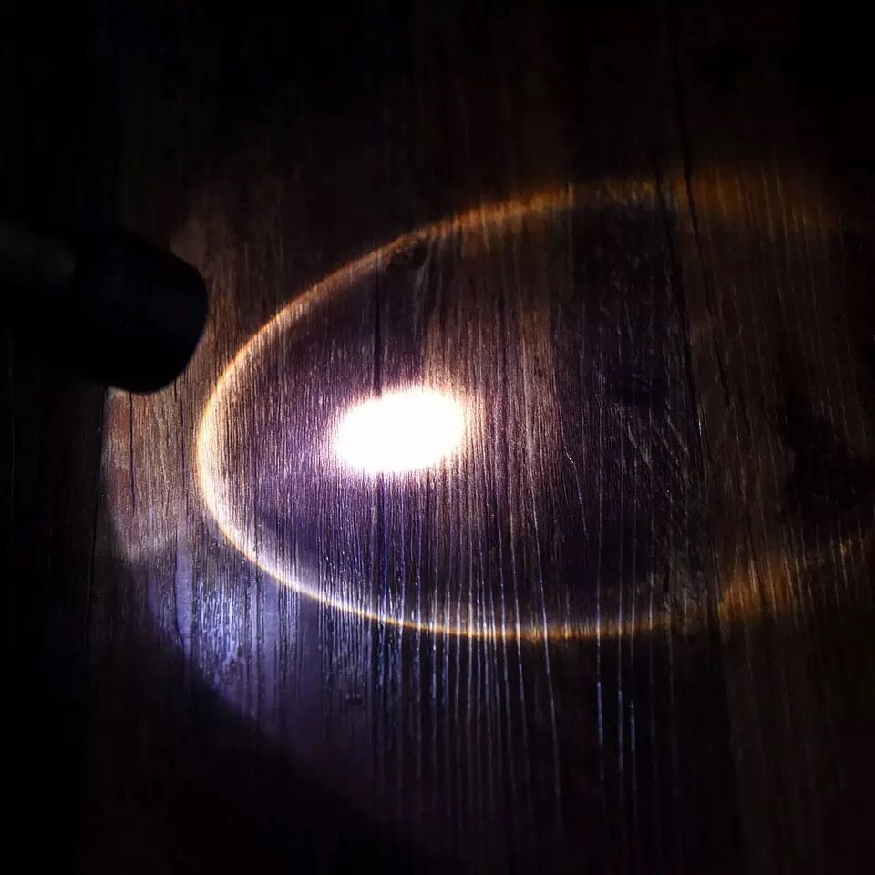 Beam of portable outdoor flashlight for camping shining bright on wooden surface in dark environment