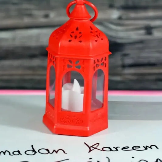 Red Ramadan lantern lamp with intricate cut-out designs and a white candle inside on a Ramadan Kareem background