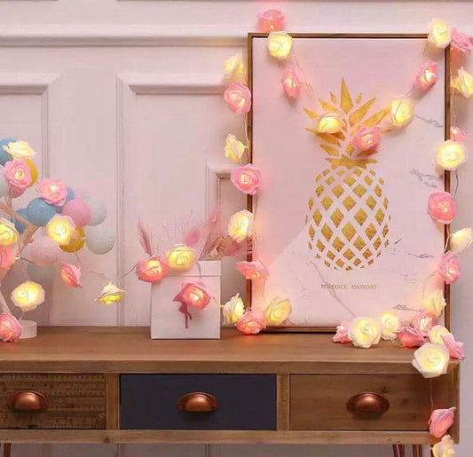 Pink and white rose fairy lights for bedroom decor draped over a wooden desk and framed pineapple artwork