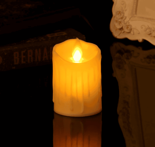 Single flickering flameless candle from a set of 12 flameless tea lights glowing softly on a reflective surface