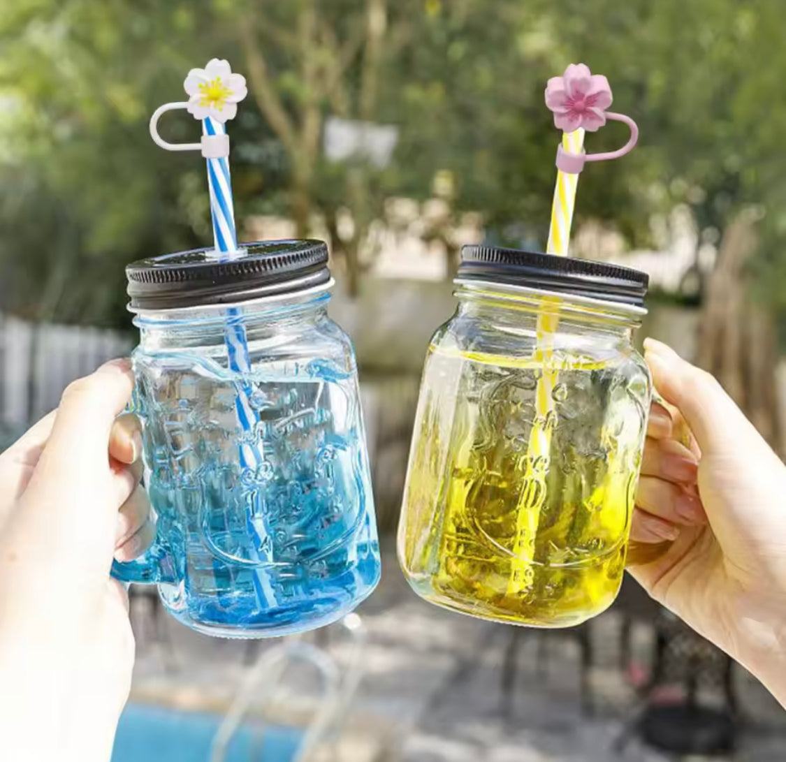 Two mason jars with black lids and colorful striped straws featuring silicone straw toppers shaped like flowers