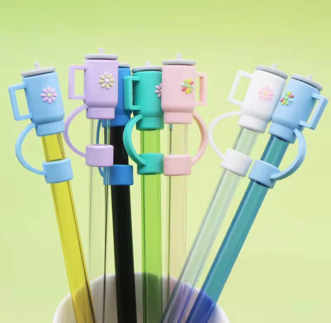 Colorful silicone straw toppers shaped like mugs on glass straws with flower designs