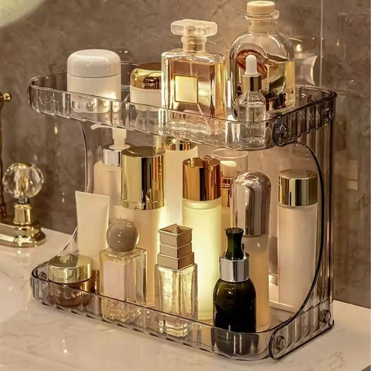Clear double layer bathroom organizer holding various skincare and perfume bottles on a marble countertop