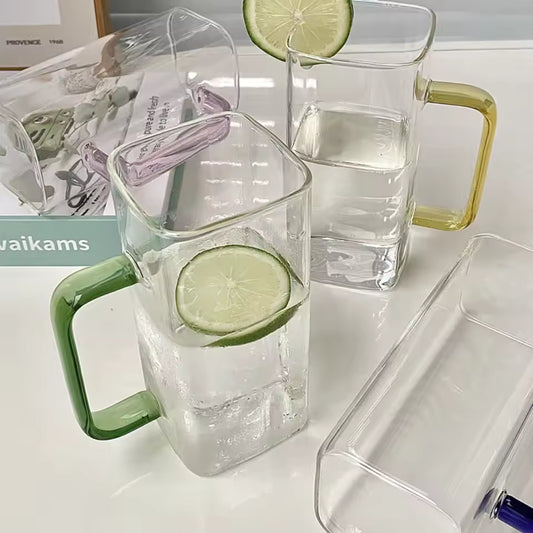 Transparent glass bottle coffee mugs with colored handles and lime slices inside on a white surface