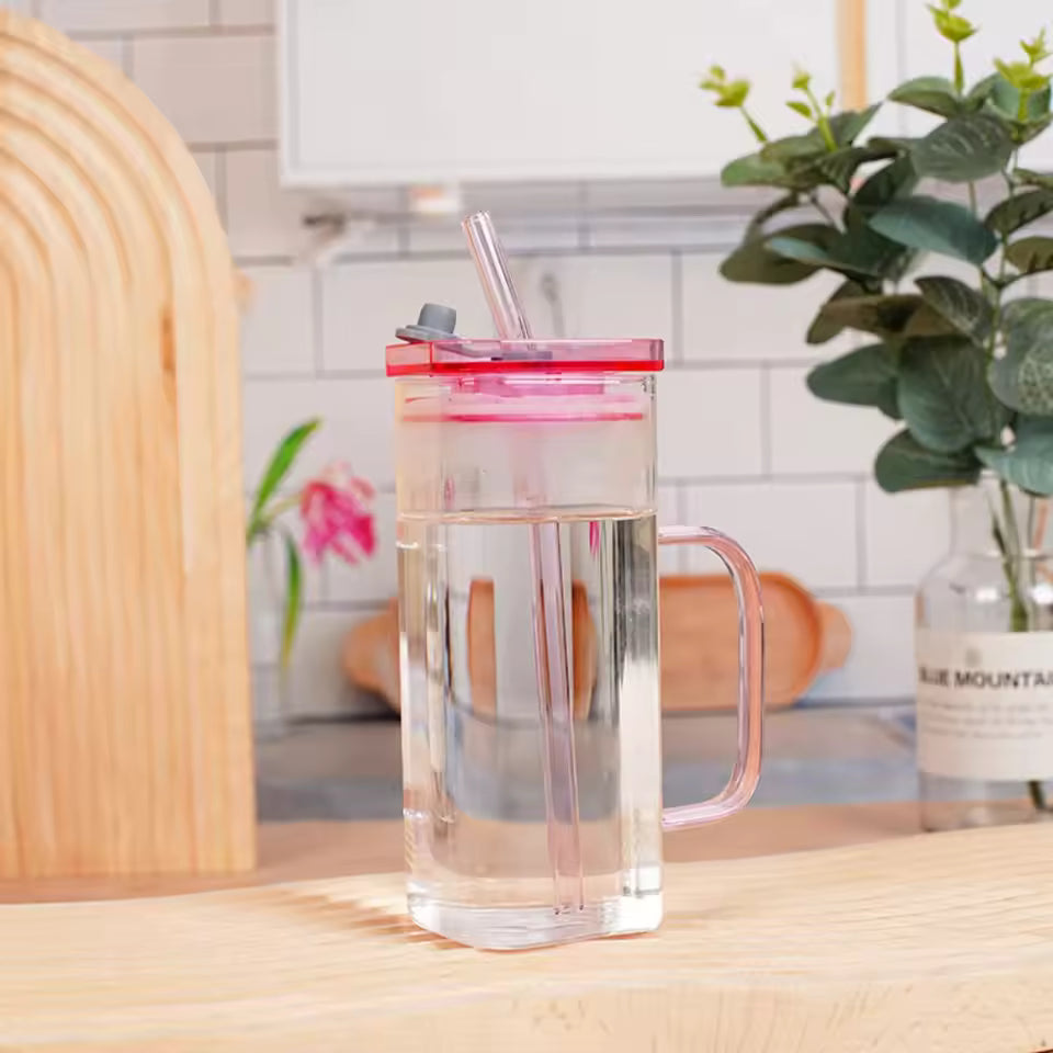 Transparent glass bottle with pink lid and straw on kitchen counter for glass coffee use