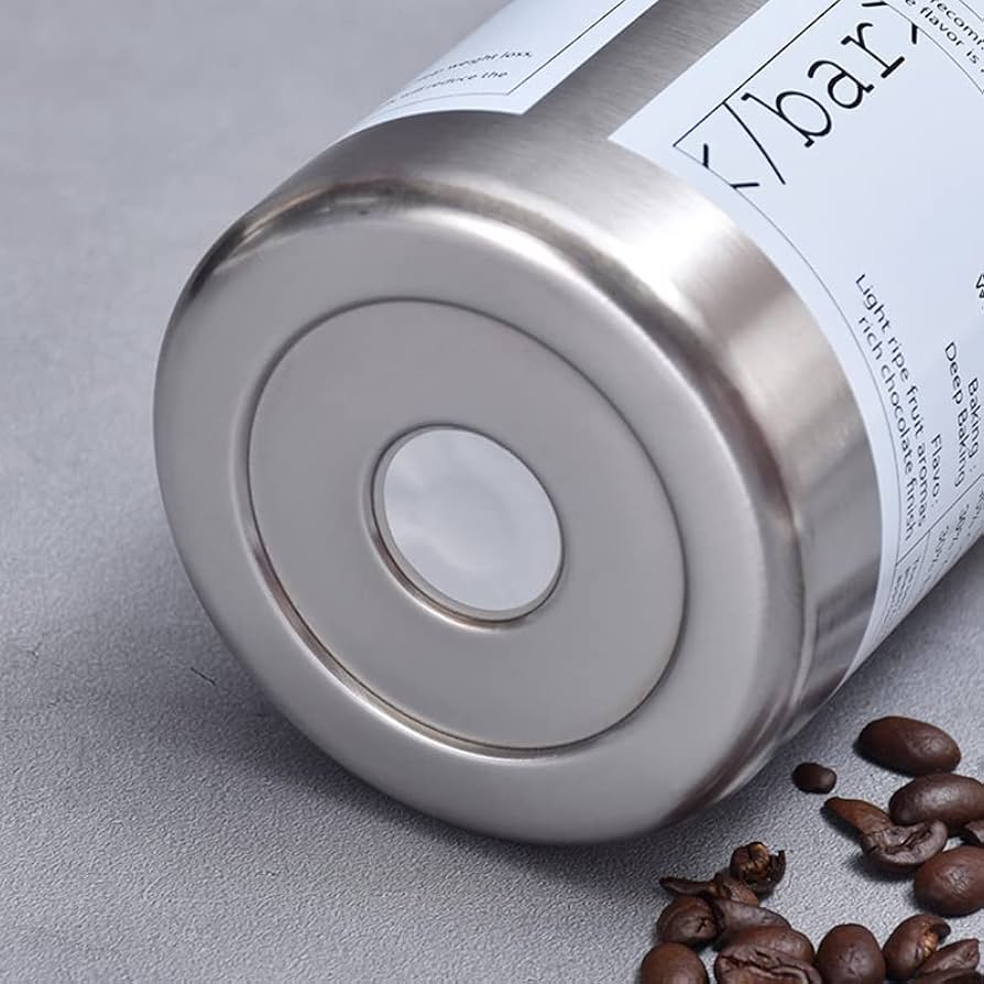 Bottom view of stainless steel coffee tumbler with coffee beans scattered on gray surface