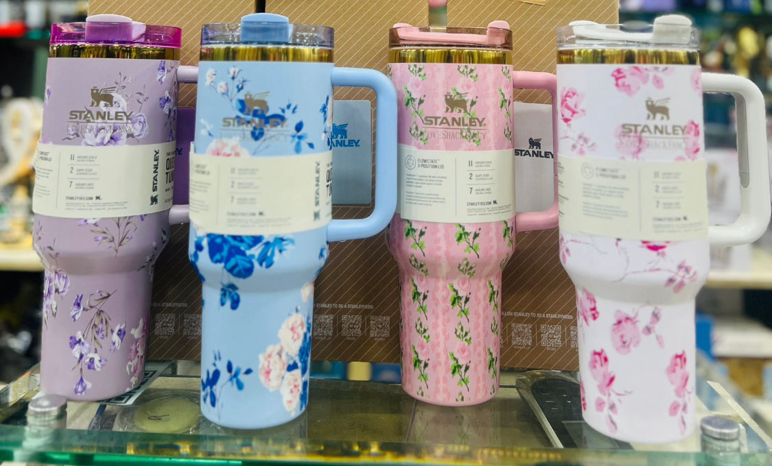 Colorful stainless steel flower tumblers with floral designs and handles displayed on a store shelf