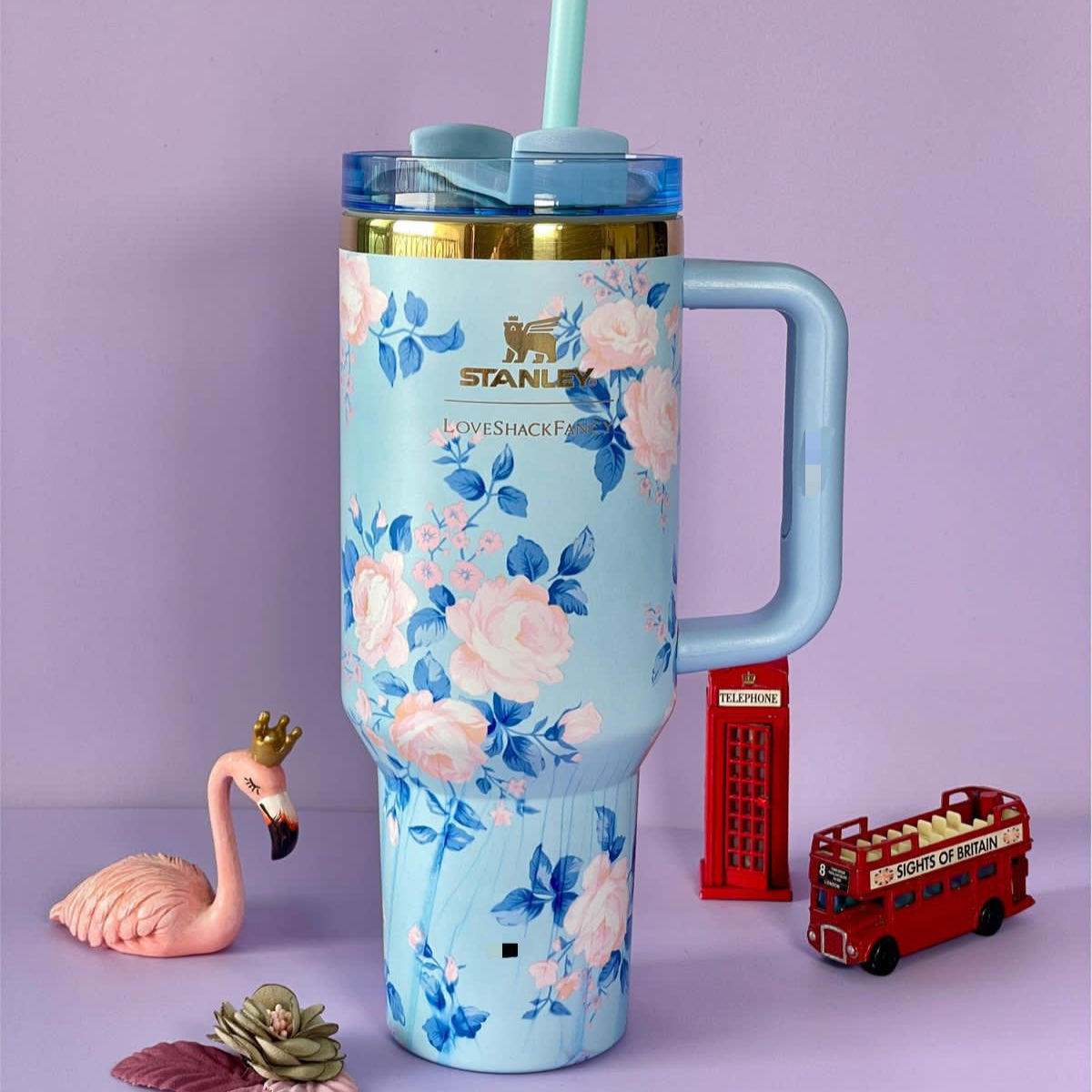 Stanley stainless steel flower tumbler with blue floral design and handle against a purple background