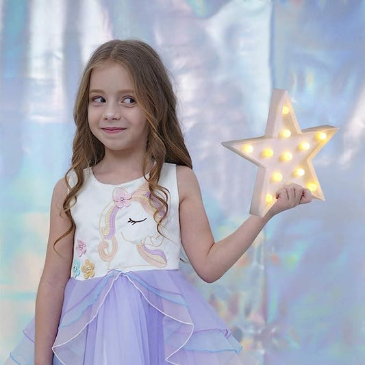 Young girl holding a star shape LED night lamp glowing with warm lights in a pastel dress