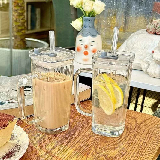Two stylish square glass mugs on a wooden table, one with tea and the other with lemon water