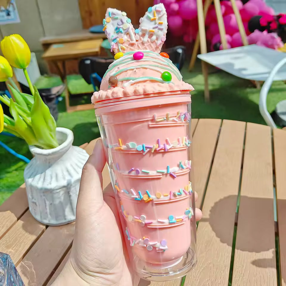 Pink unicorn water cup with straw featuring decorative sprinkles and bunny ears held outdoors