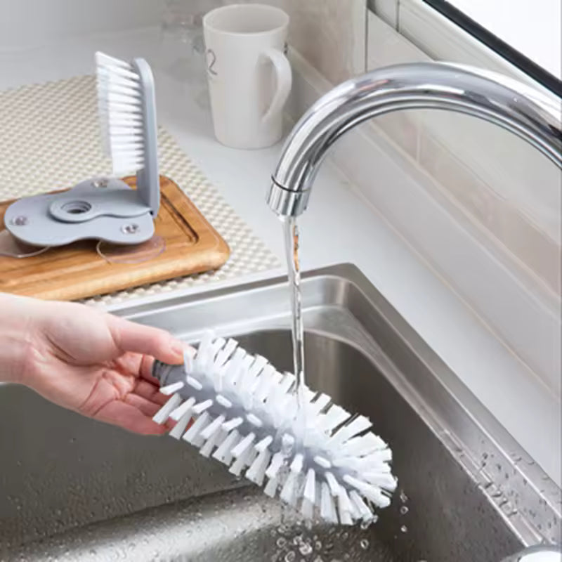 Clarify.pk sink bottle cleaning brush with white bristles being rinsed under kitchen faucet in stainless steel sink