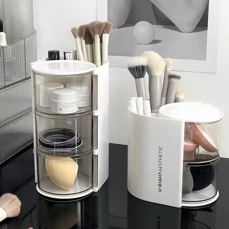 Clear and white 3 layer cosmetic storage box holding makeup brushes, sponges, and jars on a black surface
