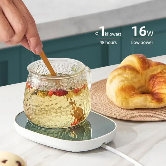 USB powered cup heater warming a glass cup of tea on a white surface with pastry nearby