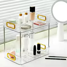 Clear acrylic vanity countertop storage tray with gold handles holding makeup and skincare items