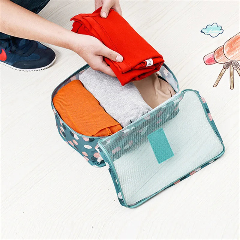 Hands packing red clothes into a blue floral travel bag from a 6 piece luggage organizer set