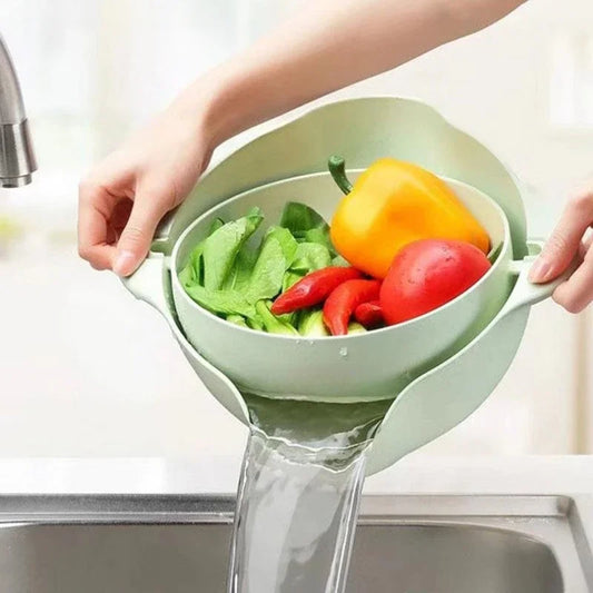 Hands holding a double layer fruit and vegetable basket with fresh produce draining water over a sink