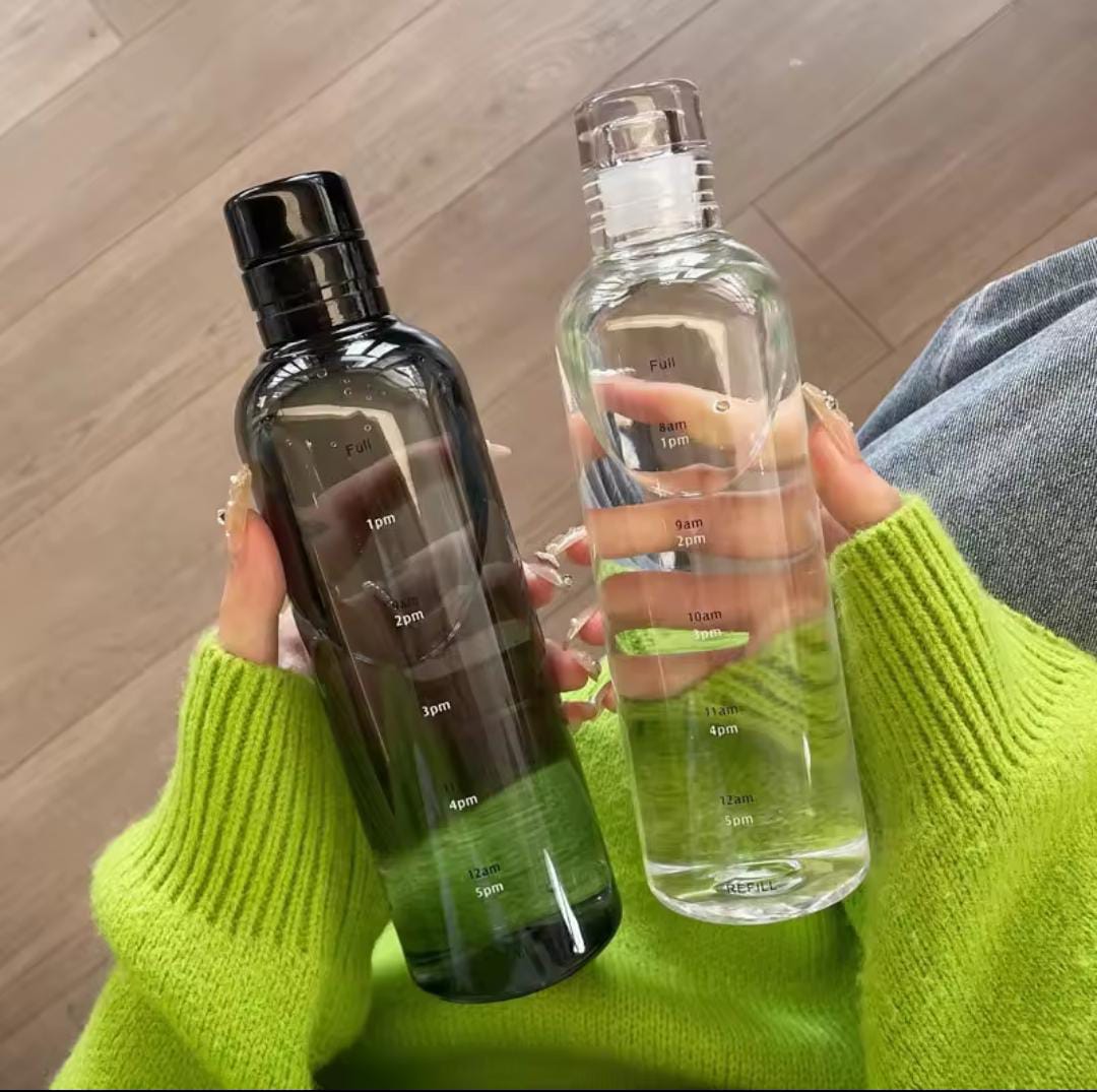 Clear and black transparent plastic water bottle 500ml with time markers held in hands over green sweater