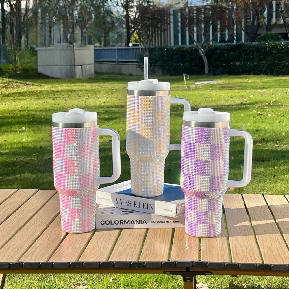 Three 1200ml Rhinestone Tumblers in pink, white, and purple checked patterns on a wooden table outdoors
