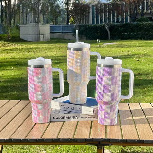 Three 1200ml Rhinestone Tumblers in pink, white, and purple checked patterns on a wooden table outdoors