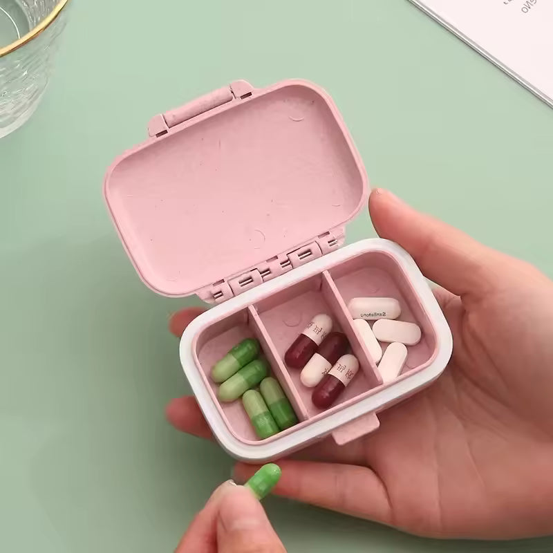 Clarify.pk 3 compartment pill box in pink held in hand with green, red, and white capsules inside