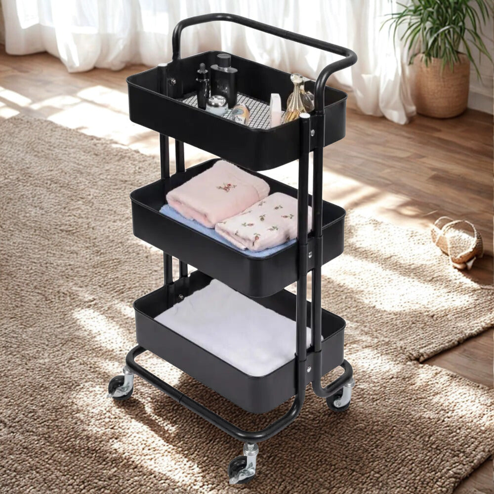 3 tier folding metal cart with wheels in black holding towels and toiletries in bright room