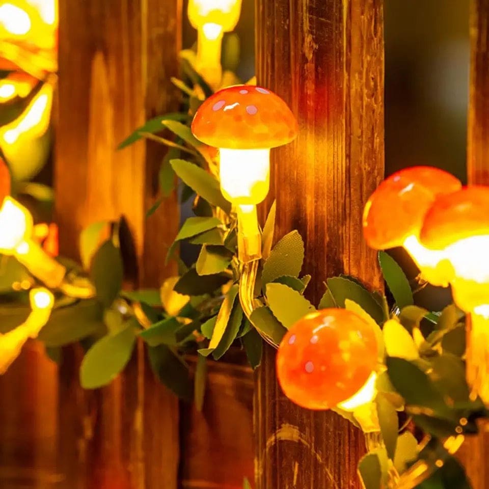 Warm glowing 3D mushroom string lights wrapped around wooden fence with green leaves decoration