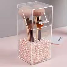 Clear acrylic cosmetic organizer with compartments holding makeup brushes and pink decorative beads