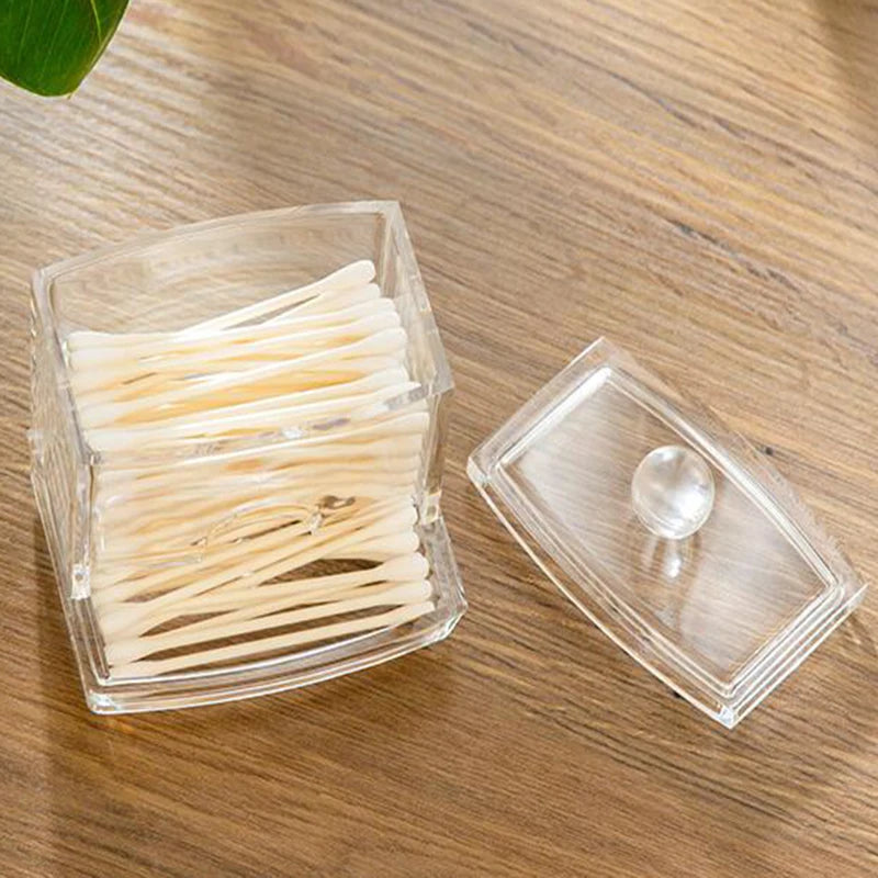 Clear acrylic cotton swab storage box with removable lid holding white cotton swabs on wooden surface