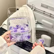 Clear acrylic hair accessories organizer box filled with purple clips near a washing machine