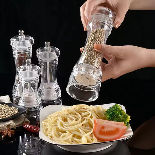 Set of clear acrylic manual paper grinder salt and pepper mills with spices being ground over pasta dish