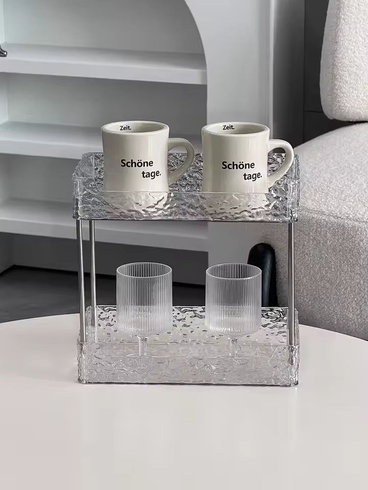 Clear acrylic shower organizer with two tiers holding two mugs and two clear glasses on a white surface