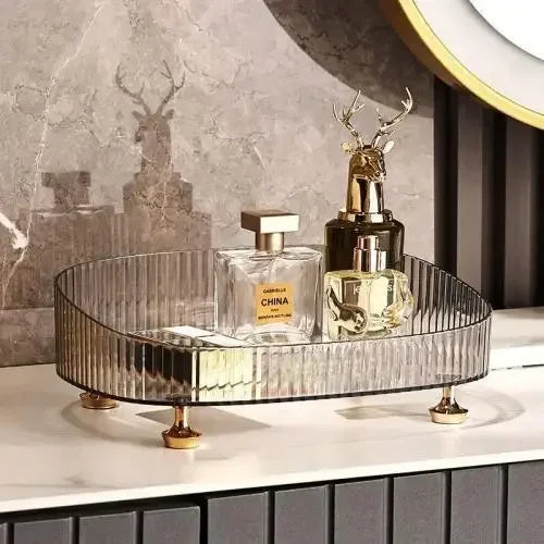 Elegant transparent dresser storage box with gold feet holding perfume bottles on a white countertop