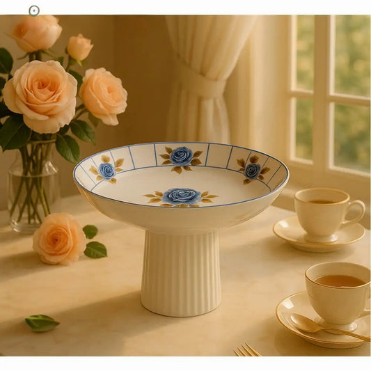 Angela Blue Rose Porcelain Pedestal Bowl with blue rose design displayed on table with tea cups and peach roses