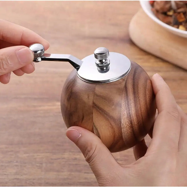 Hand holding wooden pepper grinder round walnut finish with metal crank for tabletop kitchen use