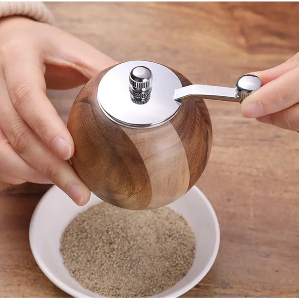 Hand cranked wooden pepper grinder with stainless steel top grinding pepper into white bowl polished wood grain