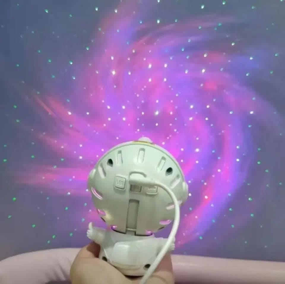 Hand holding astronaut star projector lamp projecting colorful galaxy and stars on wall