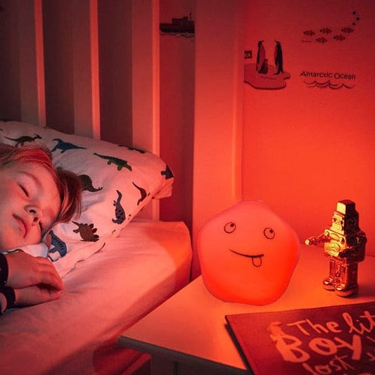 Cute baby night light silicone glowing orange on bedside table next to sleeping child