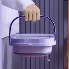 Compact purple folding washing machine with handle being carried by hand indoors