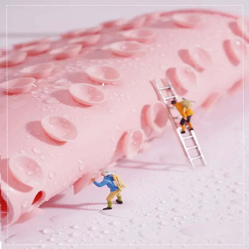 Close-up of pink silicone foot scrubber pad with water droplets and tiny figures climbing suction cups