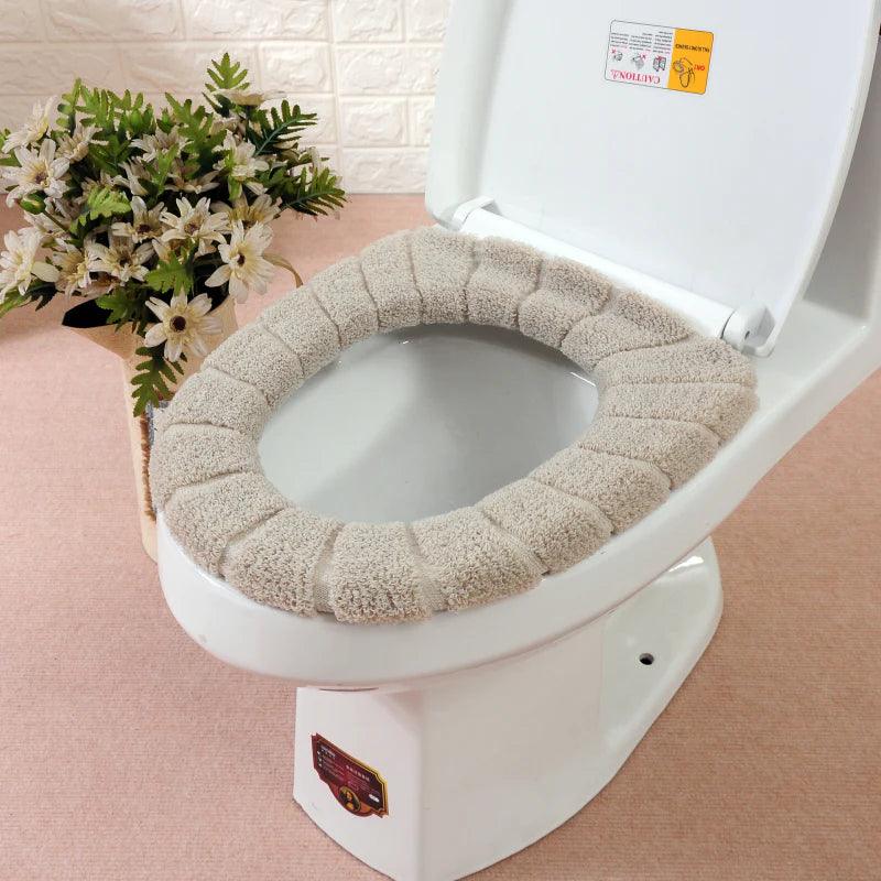 Washable toilet seat cover in beige soft fabric on a white toilet with decorative flowers nearby