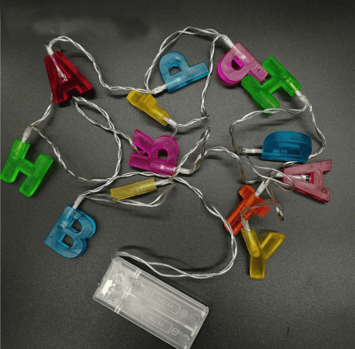 Colorful birthday decoration string lights with alphabet letters and battery pack on black background