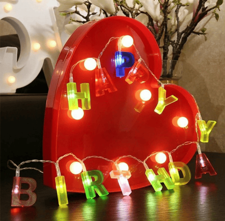 Colorful birthday decoration string lights spelling Happy Birthday with glowing bulbs on red heart background