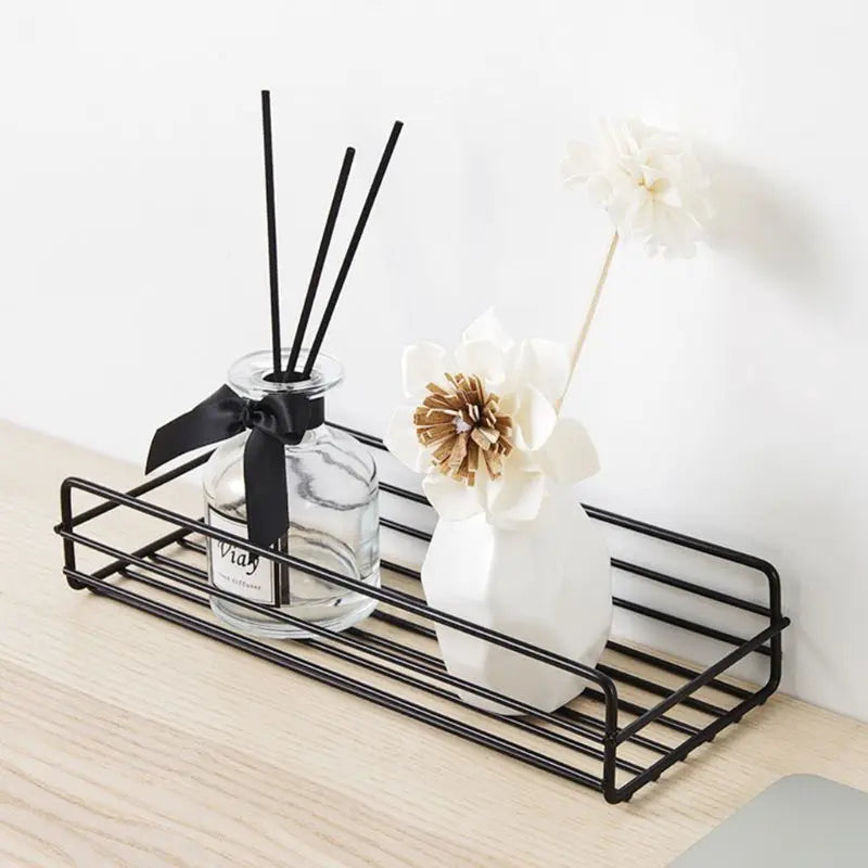 Black bathroom shelf organizer holding decorative glass bottle and white flower vase on wooden surface