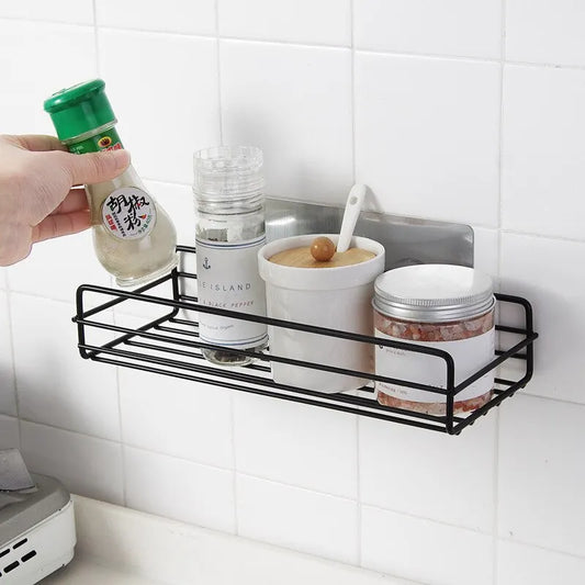 Black bathroom shelf organizer mounted on white tiled wall holding spices and condiments